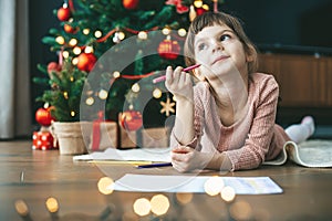 Cute little child girl writing her dreams of a gift near Christmas tree