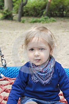 Cute little child having fun on a colorful swing outdoor in the park. Beautiful spring day in children playground