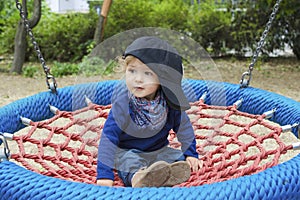 Cute little child having fun on a colorful swing outdoor in the park. Beautiful spring day in children playground