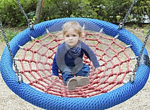 Cute little child having fun on a colorful swing outdoor in the park. Beautiful spring day in children playground