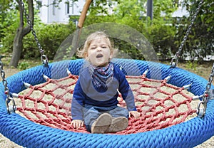 Cute little child having fun on a colorful swing outdoor in the park. Beautiful spring day in children playground