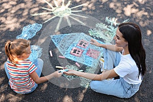 Cute little child and her mother drawing with colorful chalks on asphalt, above view