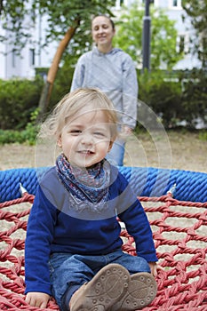 Cute little child with his mother having fun on a colorful swing outdoor in the park. Beautiful spring day in children playground