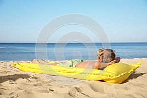 Cute little child with inflatable mattress lying at beach on sunny day