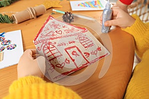 Cute little child making beautiful Christmas greeting card at wooden table, closeup