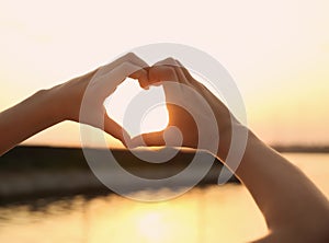 Cute little child making heart with hands outdoors at sunset