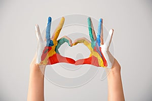 Cute little child making heart with hands in paint on light background