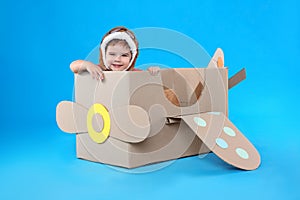 Cute little child playing with cardboard airplane on blue background