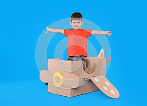 Cute little child playing with cardboard airplane on blue background