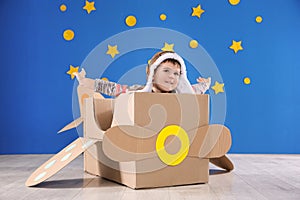 Cute little child playing with cardboard airplane near wall