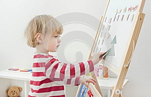 Cute little child playing at a magnetic board, learning letters, numbers and geometric shapes at home. Educative and funny indoor photo