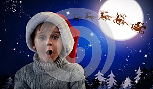 Cute little child and Santa Claus flying in his sleigh against moon sky on background. Christmas celebration