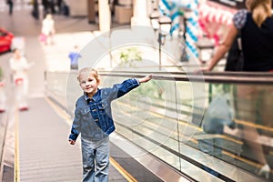 Cute little child in shopping center standing on moving escalator