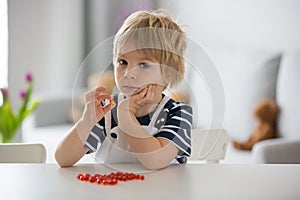 Cute little child, toddler boy, eating alfa omega 3 child suplement vitamin pills at home