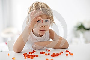 Cute little child, toddler boy, eating alfa omega 3 child suplement vitamin pills at home