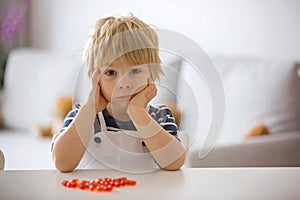 Cute little child, toddler boy, eating alfa omega 3 child supplement vitamin pills at home