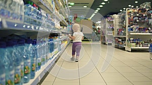 Cute little child walking in water department in the supermarket and choosing bottles inside of a big marketplace