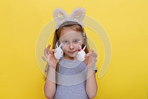 Cute little child wearing bunny ears on Easter day. Girl holding a painted egg on light yellow background. Studio photography