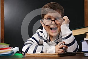 Cute child wearing glasses at desk in classroom. First time at school