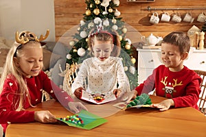 Cute little children with beautiful Christmas cards at table in decorated room