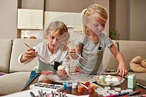 Cute little children, brother and sister painting colorful Easter eggs, sitting on a couch at home