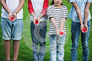 Cute little children holding red hearts while standing on green grass