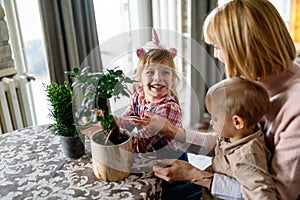 Cute little children with mother taking care of plants indoors. Family home gardening concept.