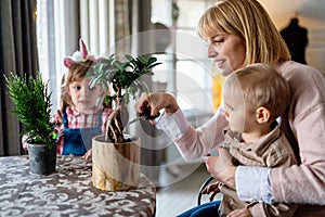 Cute little children with mother taking care of plants indoors. Family home gardening concept.