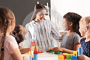 Cute little children and nursery teacher playing with building blocks in kindergarten