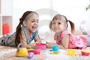 Cute little children playing with kitchenware while lying on floor at home