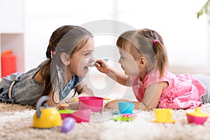 Cute little children playing with kitchenware while lying on floor at home