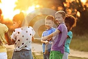 Cute little children playing tug of war game in park at sunset