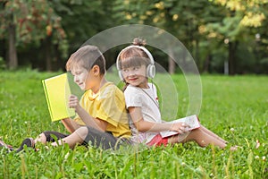 Cute little children reading books and listening to music in park on summer day