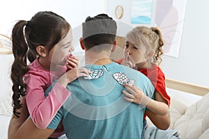 Cute little children sticking paper fish to father`s back at home