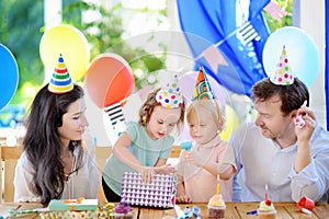 Cute little children twins and their parents having fun and celebrate birthday party with colorful decoration and cake.