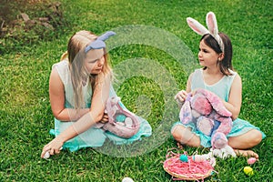 Cute little children wearing bunny ears on Easter day sitting on grass in garden. Girls holding painted eggs cover their