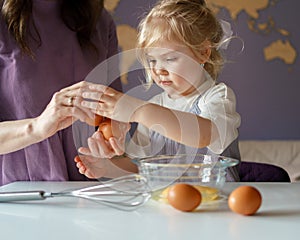 Cute little chld helping mom to cook, girl breaking eggs into bowl