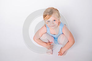 Cute little chubby girl in a blue dance leotard sitting on a white background looking up from the bottom