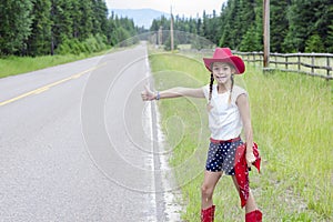 Cute little cowgirl trying to hitch hike a ride on a lonely road