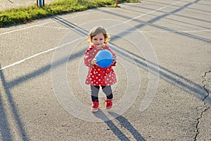 Cute little curly baby girl with ball in her hands on the stadium