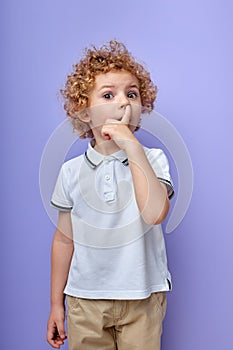cute little curly boy picking his nose to explore it and act mischievous for fun
