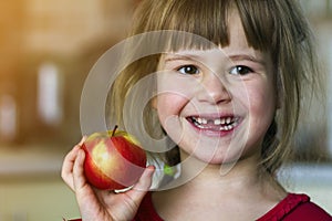 A cute little curly toothless girl smiles and holds a red apple. Portrait of a happy baby eating a red apple. The child loses milk