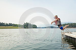 Cute little daring boy jumping off the boat dock at the lake. Being adventurous