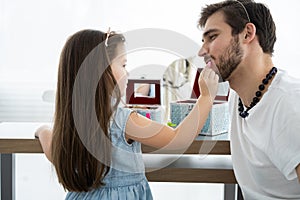 Cute little daughter and her handsome young dad in crowns are playing together in child`s room. Girl is doing her dad a