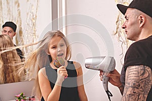 Cute little daughter and her tattoed dad are playing together near a mirror. Dad is doing his daughter`s hair. Family