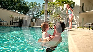 Cute little daughter and his father swimming in the pool. The father is holding his daughter in his hands and embracing