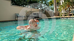 Cute little daughter and his father swimming in the pool. The father is holding his daughter in his hands and embracing.