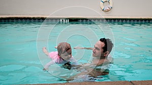 Cute little daughter and his father swimming in the pool. The father is holding his daughter in his hands and embracing