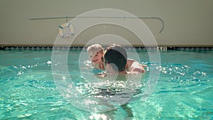 Cute little daughter and his father swimming in the pool. The father is holding his daughter in his hands and embracing