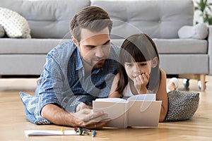 Cute little daughter listening to dad reading book at home